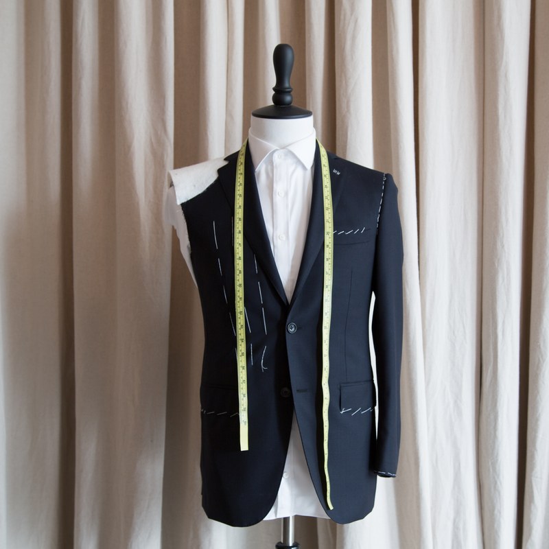 A basted navy jacket on a stand with a tape measure, ready for a fitting
