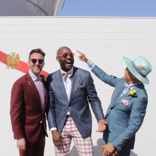 Carl in a burgundy suit with two friends in tailoring at the Melbourne Cup, beside a Mumm marquee
