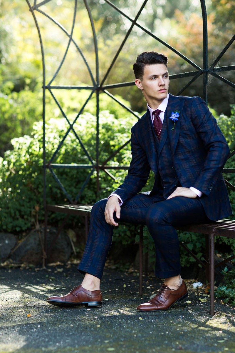 A model in a navy three-piece suit seated in a Melbourne garden pavilion