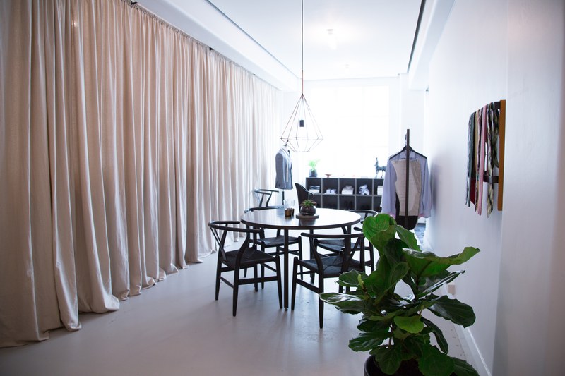 The tailoring studio: linen curtains, a round table with timber chairs and a jacket on a stand