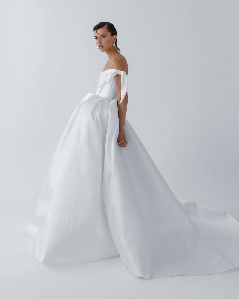 Model in an off-the-shoulder Elly Sofoclí ball gown with a long train