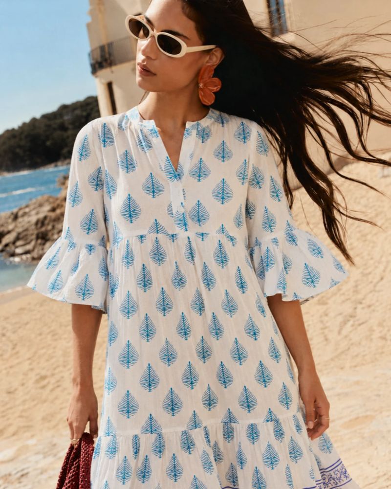 A model in a blue and white printed dress on a beach
