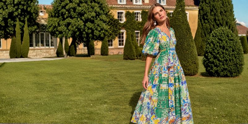 A model in a printed maxi dress on a lawn in front of a country house