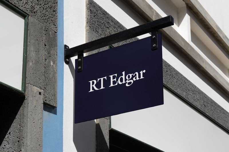 A hanging RT Edgar sign in navy with the white wordmark, on a concrete building